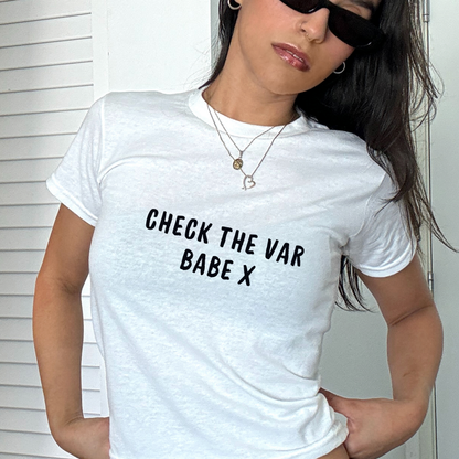 White fitted baby tee with black “Check The VAR Babe X” slogan, styled casually with a shoulder bag, ideal for football match days and sporty outfits