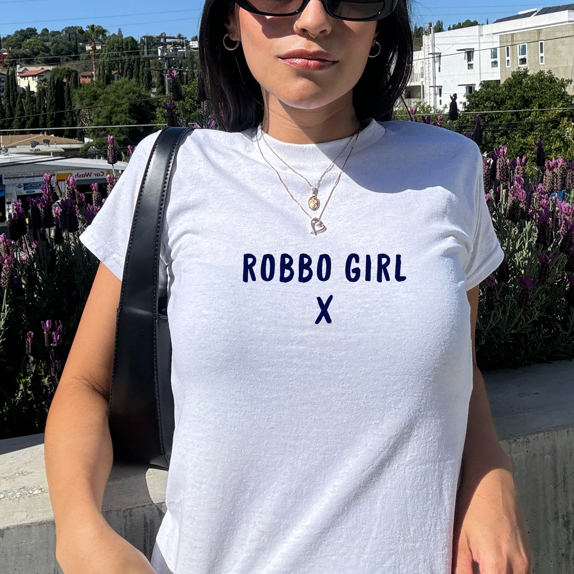 White fitted baby tee with navy “Robbo Girl X” slogan, styled casually with a shoulder bag, perfect for football fans and match day outfits