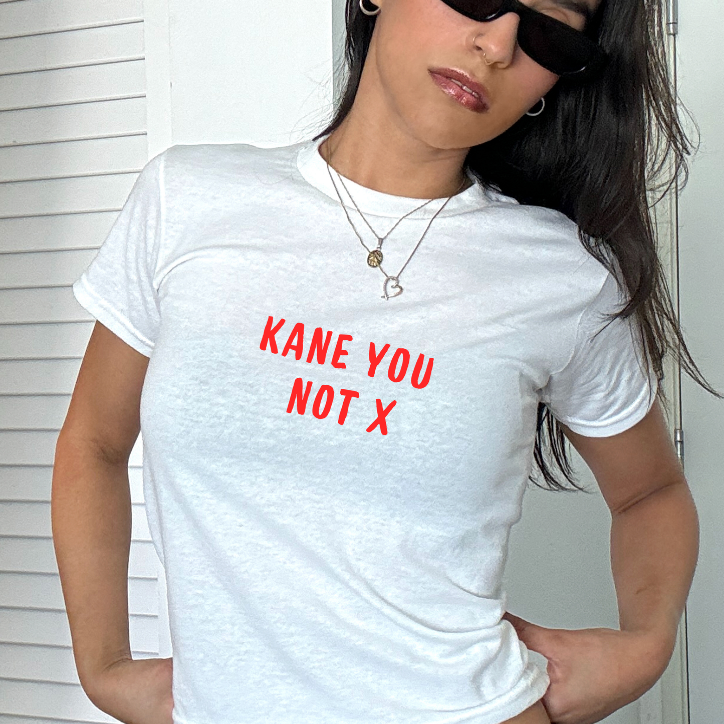 White fitted baby tee with red “Kane You Not X” slogan, styled casually with a shoulder bag, perfect for England football fans and match day outfits