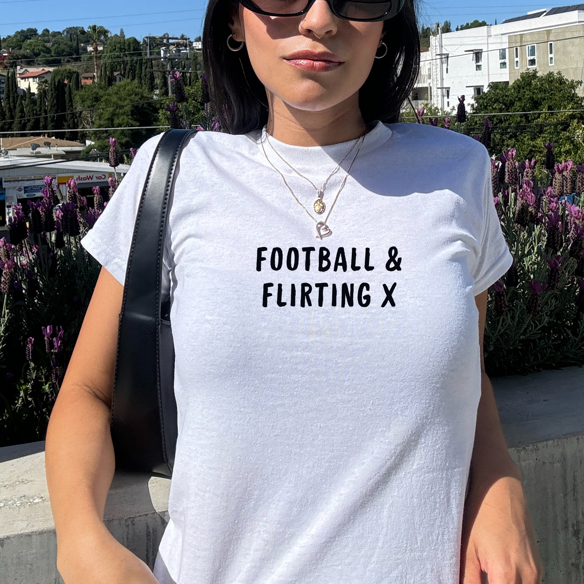 White fitted baby tee with black “Football & Flirting X” slogan, styled casually with a shoulder bag, perfect for match days and girls’ football outfits