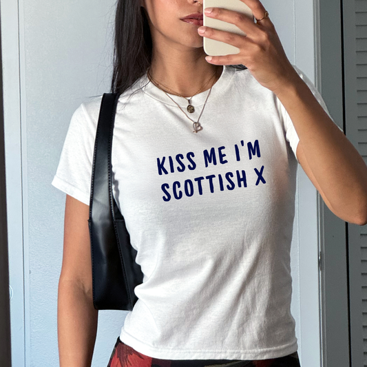 White fitted baby tee with navy “Kiss Me I’m Scottish X” slogan, styled casually with a shoulder bag, perfect for Scotland football fans and match day outfits