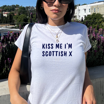 White fitted baby tee with navy “Kiss Me I’m Scottish X” slogan, styled casually with a shoulder bag, perfect for Scotland football fans and match day outfits