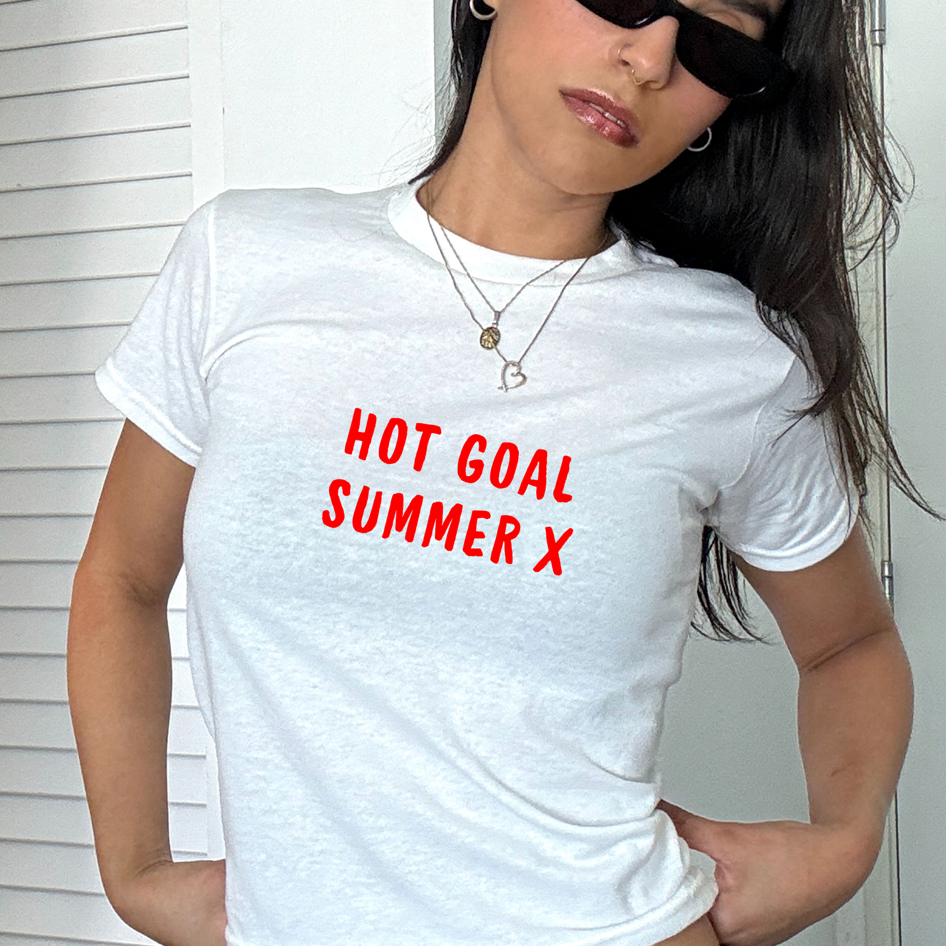 White fitted baby tee with bold red “Hot Goal Summer X” slogan, styled casually with a shoulder bag, ideal for summer football outfits and match days